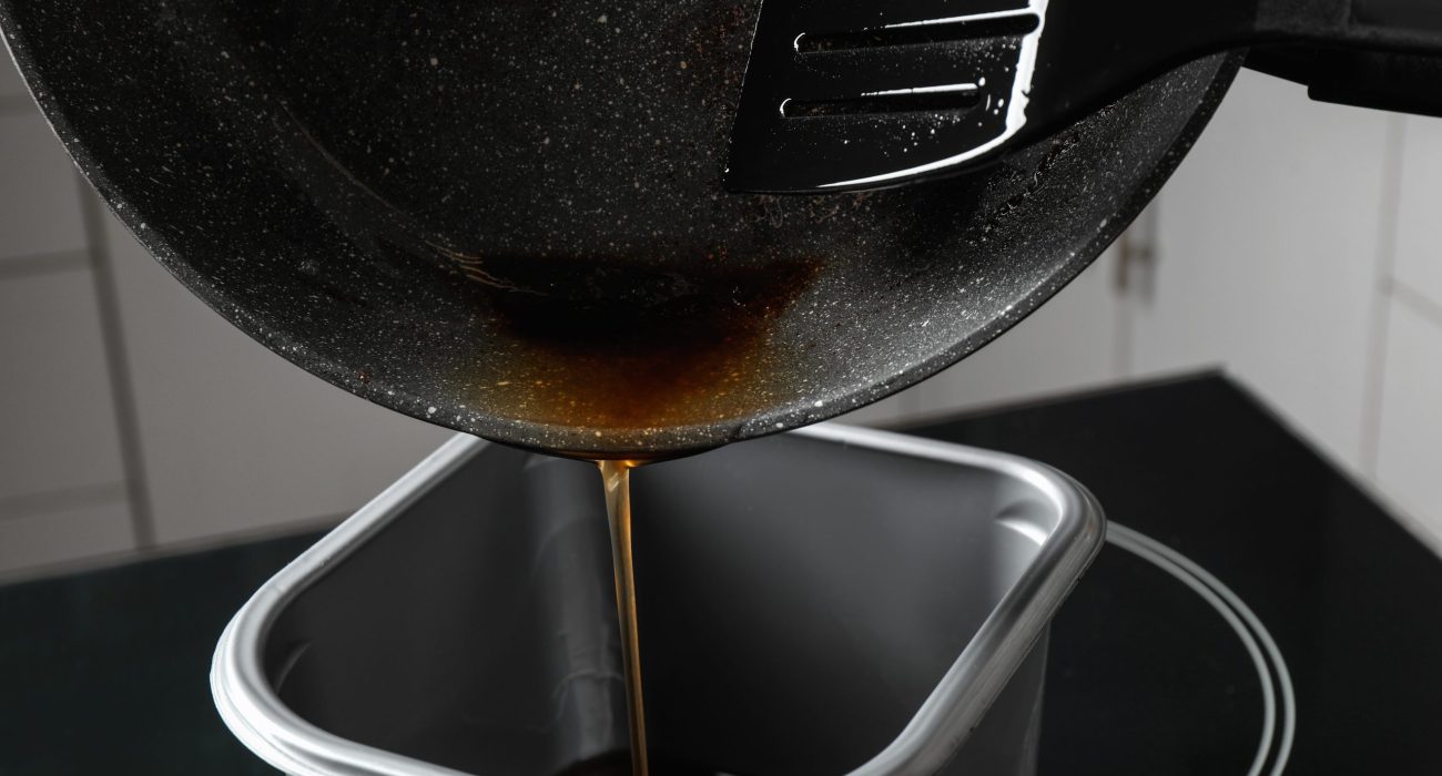 Pouring used cooking oil from frying pan into container, closeup